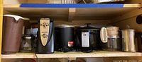 Shelf view showing multiple vintage kitchen appliances including slow cookers, a popcorn popper, coffee makers, and a plastic pitcher.