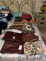 Several vintage ladies purses and totes laid out on a bed, showing different materials such as leather, wicker, and floral fabric.