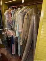 Two racks of ladies clothing showing outerwear, nightwear, and tops in various colors and materials with some garments protected in plastic.