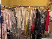 Full rack of women's clothing including sweaters, dresses, and robes, many covered in plastic garment bags.