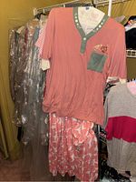 Front view showing pink top with green trim and pocket, pink and white pants, and several garments on hangers.