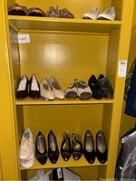 Yellow shelving unit with two shelves holding various women's shoes including heels, flats, sneakers, and slip-ons in multiple colors.
