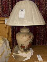 Full view of Asian-style ceramic table lamp with beige shade, showing floral and bird design on ceramic base