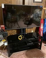 LG flat screen TV turned off on black glass TV stand in room with wood paneling.