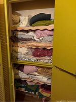 Wide view of shelves inside a yellow cabinet filled with folded linens and towels in multiple colors and materials.