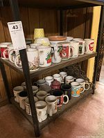 Shelf showing approx. 30 coffee mugs of various vintage designs including Coca-Cola and floral prints, some with visible dirt.