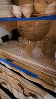 View of large clear punch bowl with matching punch cups, candy dish, and some white china teacups and saucers above on shelf