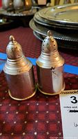Front and side view of the two sterling silver salt and pepper shakers, showing their pierced tops and cylindrical shape with signs of tarnish and wear.