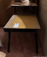 Pair of vintage 2-tier end tables with rectangular tabletops, black frames, and tapered legs, showing signs of dings, scratches, and discoloration.