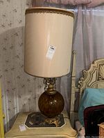 Full view of amber glass base lamp with beige shade on side table