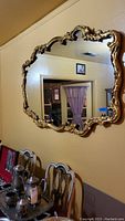 Full view of large ornate wall mirror mounted on a wall above chairs, showing the overall size, shape, and design.