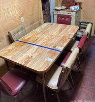 Full view of vintage rectangular kitchen table with 6 assorted red and beige padded dining chairs.