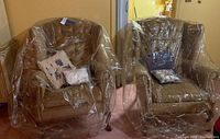 Pair of wingback chairs covered in plastic with accent pillows on each chair