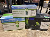 Three boxes of toner cartridges placed on a floor, two from Sustainable Earth and one Premium toner cartridge for HP.