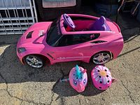 Front side view of the Barbie Corvette ride-on car with two helmets positioned in front, displayed outdoors on pavement.