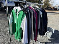 Full rack of 10 hoodies and sweatshirts shown from side on a garment rack outside in daylight.