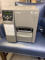 Front view of Zebra Stripe S4M label printer showing front LCD, control buttons, and branding.