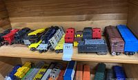 Model train cars and cabooses arranged on a wooden shelf, various colors and brands visible.
