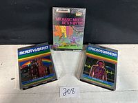 Three Intellivision game boxes displayed: Mr. Basic Meets Bits 'N Bytes sealed upright in center, Beauty and the Beast and Micro Surgeon lying flat on each side.