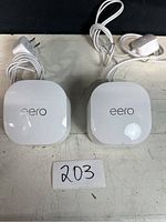Two white Eero 6+ routers with their power adapters on a white surface, front top view showing 'eero' logo.