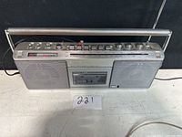 Front angle photo showing Sony silver boombox with carrying handle, speakers, cassette deck, and control knobs and buttons.