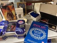 Wide view showing Hallmark Star Trek communicator box, Bakugan packaging with figures, Space Art Fantastica trading cards box, Star Wars book, anime figure box, and small collectible boxes.