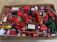 Full view of the box containing various toy fire trucks, mostly red with a few other colors such as green and orange.