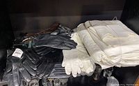 View showing multiple pairs of women's leather gloves in black, brown, and white color, some with tags, alongside folded white bed sheets