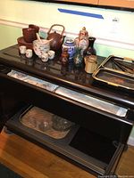 Asian brown ceramic teapots and cups alongside blue and brown vases, ginger jars, and trays on a lacquered black wooden surface.