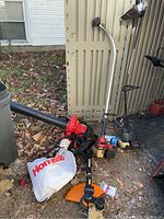 Photo showing the lot outdoors with all three tools visible: a red and black Homelite blower/vac with white bag, a Worx edger with orange trimming guard, and a Craftsman edger with red engine cover.