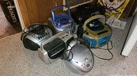 Six boomboxes grouped on floor, various sizes, styles and colors, some with visible CD and cassette decks