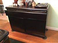 Front and left angled view of black lacquered buffet showing drawer and doors with scratches visible on surface.