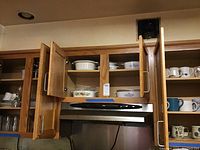 Upper kitchen cabinets open showing Corning bakeware dishes, Pyrex measuring cups, and Corelle dishes inside