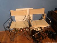 Two matching folding chairs with metal frames and beige canvas seats and backs next to a blue wall on wooden floor.