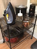 Sunbeam iron, Montgomery Ward blender, Presto electric kettle, electric can opener, Hamilton Beach slow cooker, two-slice toaster on metal shelving unit