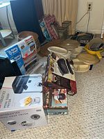 Various boxed and unboxed kitchenware items including Ambiano Mini Deep Fryer, bakeware, and food storage containers on carpet floor