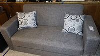 Front view of gray fabric loveseat with two circular pattern pillows on seat, showing clean upholstery and cushion top surface.