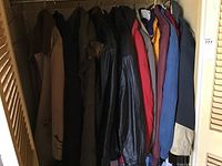 Full view of nine men's coats and jackets hanging on a rack, showing various colors and styles from leather to insulated winter jackets.
