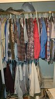 Closet rack with assorted men's shirts hanging closely, mix of plaid flannel, casual, button-up long and short sleeve shirts in various colors.