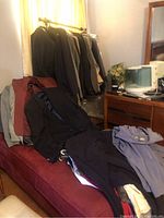 Various men's suits, jackets, and folded clothing stacked on red bench near clothing rack.