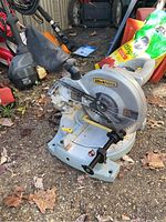 Side view of the gray and silver WorkForce compound miter saw with dust bag on the ground outdoors.