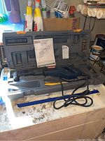 RYOBI reciprocating saw with electric cord inside grey plastic case, manual placed on top.