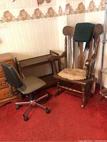 Shows wooden rocking chair with beige cushion and green blanket, gray office chair, and black rolling cart near wooden dresser.