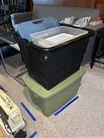 Set of four storage bins stacked: black with lid open on top of green Cornerstone 18 gallon tote with lid. Inside the black bin is a smaller clear bin with lid and a small bin without lid.