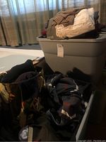 Photo showing three plastic tubs filled with assorted sweaters and socks in mixed colors and fabrics.