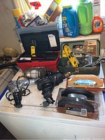Photo showing assortment of tools including Black and Decker drill, hand trowels, toolboxes with supplies, heat tool, and shop light.