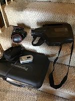 Panasonic PV 704 VHS camcorder with carrying case, charger, and light laid out on carpeted stairs