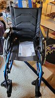 Front view of folding wheelchair showing padded black fabric seat, backrest, armrests and user manual on the seat