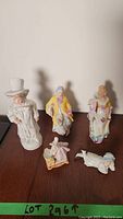 Five Victorian style porcelain figurines displayed on a wooden surface.