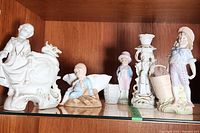 Full view of five antique/vintage porcelain figurines and match holders on a shelf